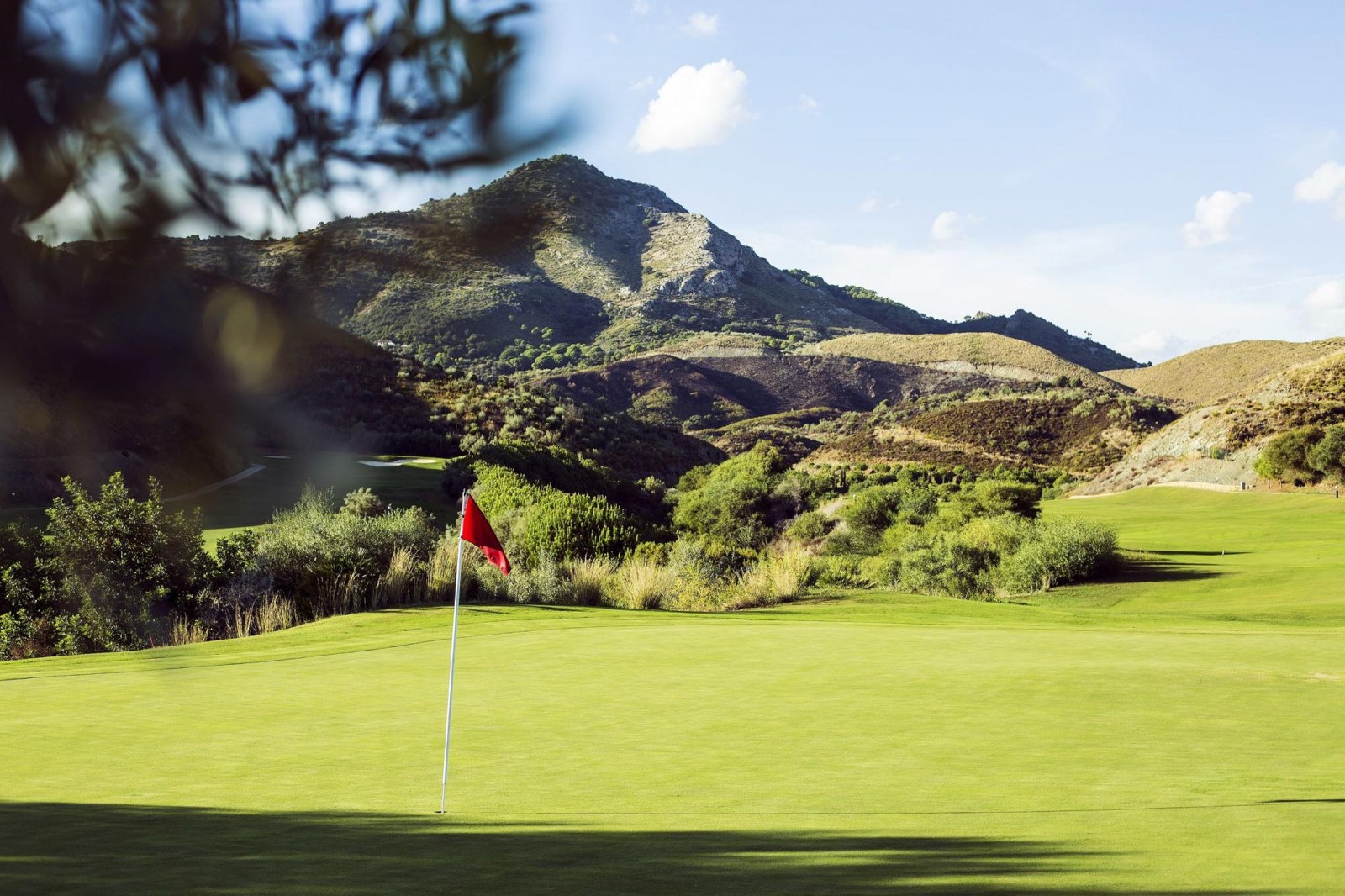 Green con bandera roja y montañas al fondo en Alferini Golf, Villa Padierna, Benahavís, Málaga